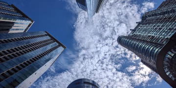 Looking up at modern skyscrapers under a blue sky with dramatic clouds.