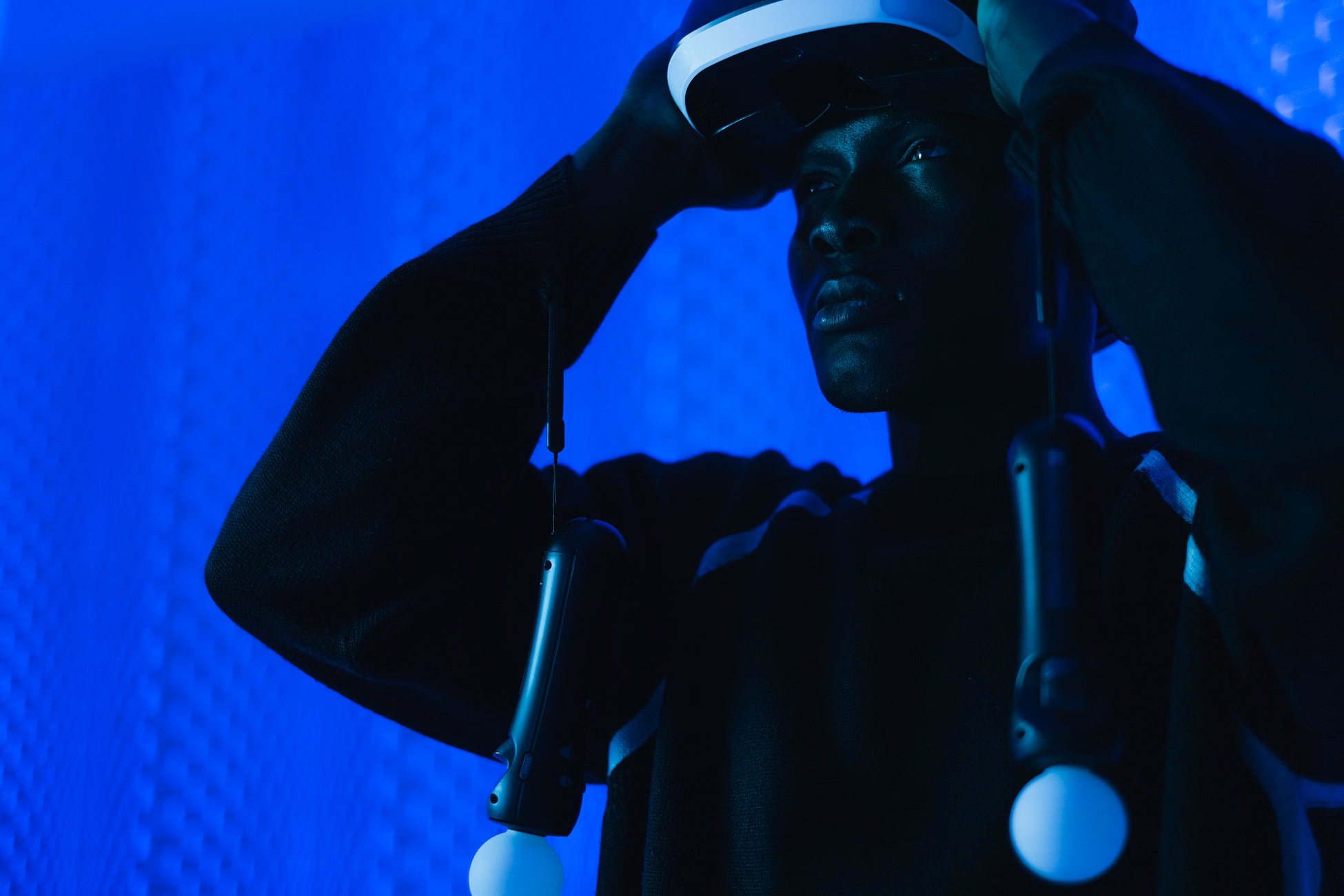 A man immerses in virtual reality using a VR headset and controllers in a tech-themed room.