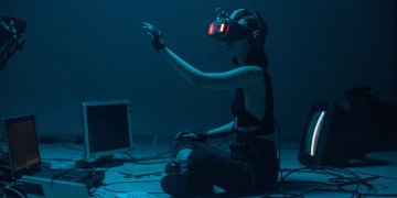 Woman immersed in virtual reality, surrounded by tech, in a dimly lit room.