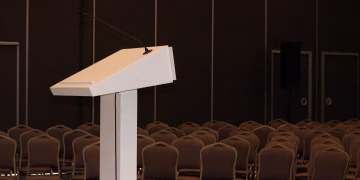 An empty conference room setup with podium and rows of chairs, ready for an event.