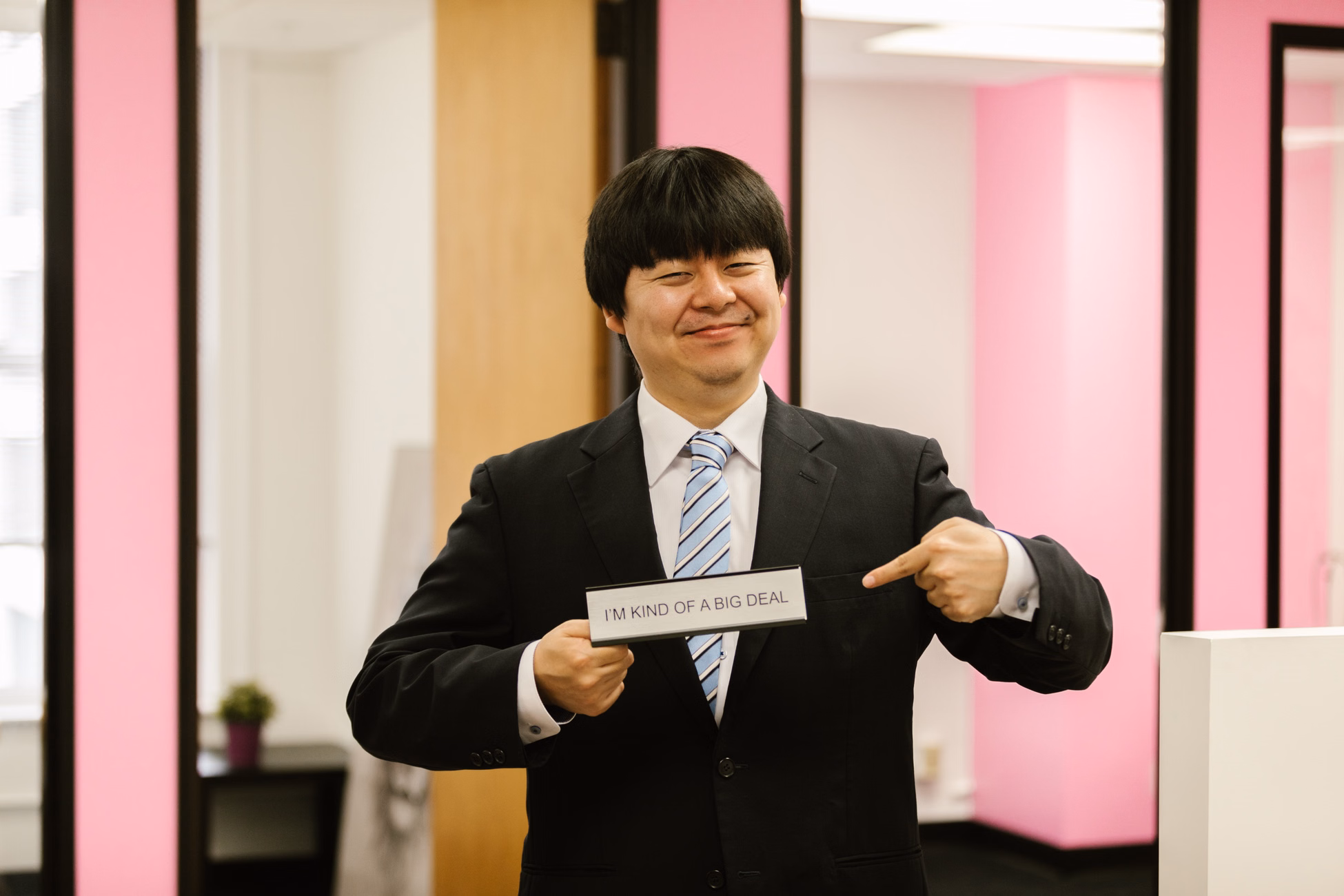 Asian businessman confidently holding funny office sign, showcasing humor in business attire.