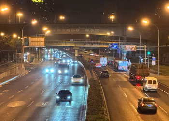 Traffic flows along a major Beijing highway, illuminated by bright streetlights at night.