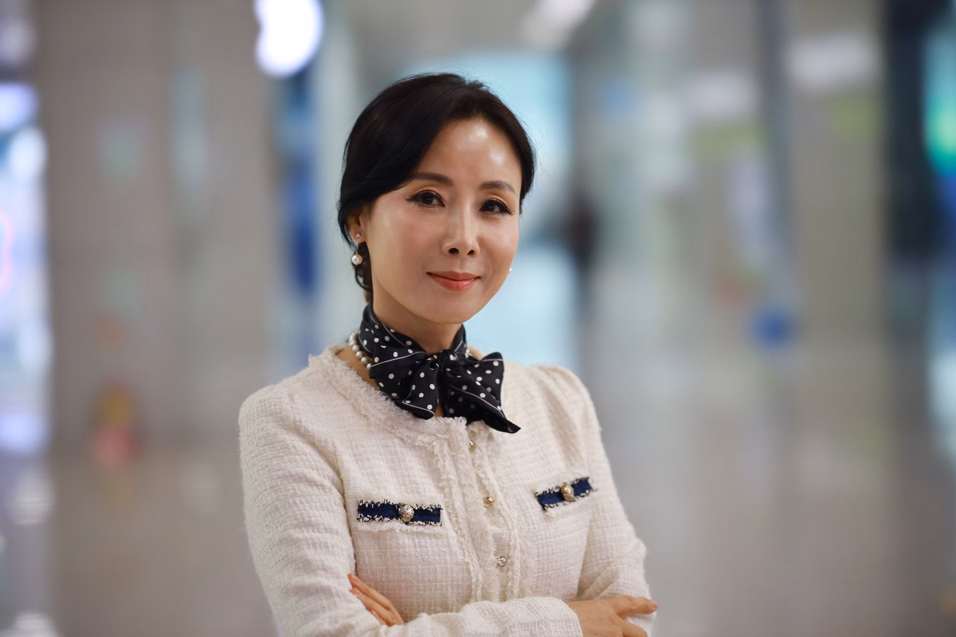 A sophisticated woman smiles confidently in a stylish outfit indoors, exuding elegance and charm.