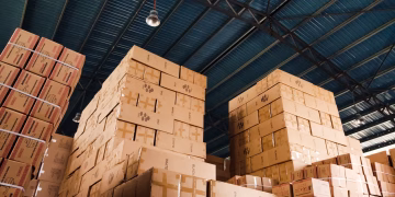 High stacks of cardboard boxes organized in a warehouse with a blue metal ceiling.