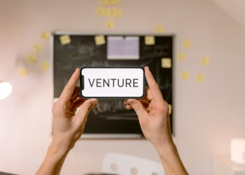 A smartphone displaying 'Venture' held by hands in an office setup. Ideal for business and startup themes.