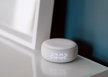 Close-up of a smart speaker with an illuminated 20:02 LED clock display on a desk.