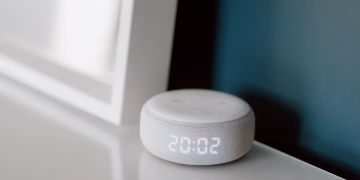 Close-up of a smart speaker with an illuminated 20:02 LED clock display on a desk.