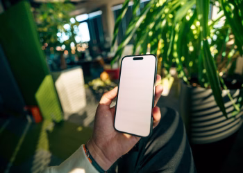 A person holding a smartphone with a blank screen in a plant-filled contemporary office setting.