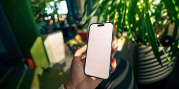 A person holding a smartphone with a blank screen in a plant-filled contemporary office setting.