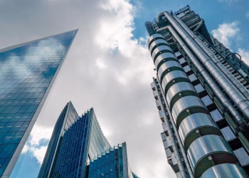 Low angle view of futuristic skyscrapers in London's financial hub under a partly cloudy sky.