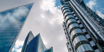 Low angle view of futuristic skyscrapers in London's financial hub under a partly cloudy sky.
