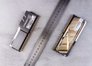 Close-up of computer memory modules and metal ruler placed on a textured gray surface.