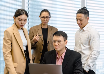 Group of professionals gathered around a laptop for a work meeting in a modern office.