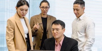 Group of professionals gathered around a laptop for a work meeting in a modern office.