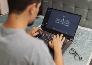 Man using laptop with AI interface, typing with focused attention. Indoors with eyewear beside.