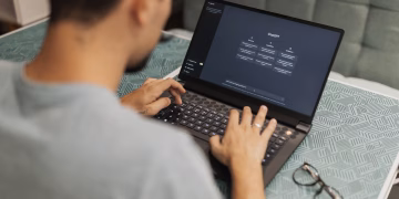 Man using laptop with AI interface, typing with focused attention. Indoors with eyewear beside.