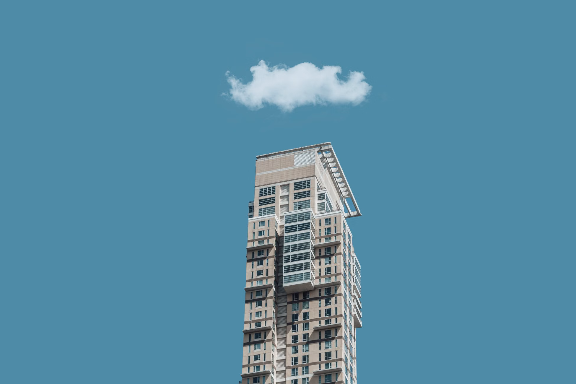 Low-angle shot of a modern high-rise building against a clear sky with a single cloud above.