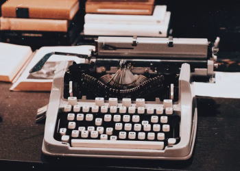 Close-up of an antique typewriter on a desk surrounded by books, evoking a classic retro style.