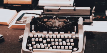 Close-up of an antique typewriter on a desk surrounded by books, evoking a classic retro style.
