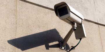 Modern surveillance camera mounted on a concrete wall casting a shadow.