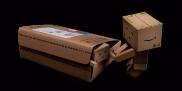 Whimsical cardboard robot figure emerging from a shipping box on a black background.