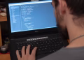 Man working on code on a laptop in an office, showcasing modern remote work setup.