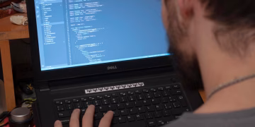 Man working on code on a laptop in an office, showcasing modern remote work setup.