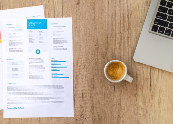 Top view of a desk with resume, coffee cup, and laptop on a wooden surface, ideal for business concepts.