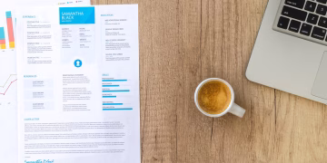 Top view of a desk with resume, coffee cup, and laptop on a wooden surface, ideal for business concepts.