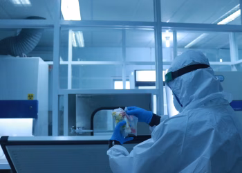 Lab technician in full protective suit performs tasks in a controlled laboratory environment.