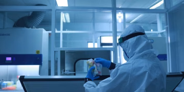 Lab technician in full protective suit performs tasks in a controlled laboratory environment.