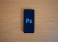 Top view of a smartphone showing Adobe Photoshop on a wooden surface.