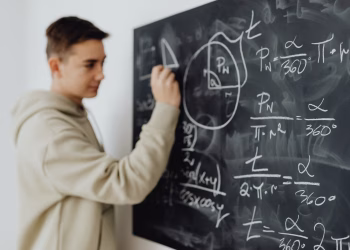 Focused teenager solving a math equation on a blackboard in a classroom setting.