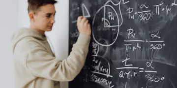 Focused teenager solving a math equation on a blackboard in a classroom setting.