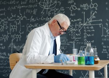 Scientist in lab coat working at desk with formulas.
