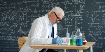 Scientist in lab coat working at desk with formulas.