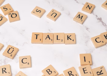 Wooden Scrabble tiles on a marble background spelling 'Talk', symbolizing communication and language.