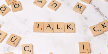 Wooden Scrabble tiles on a marble background spelling 'Talk', symbolizing communication and language.