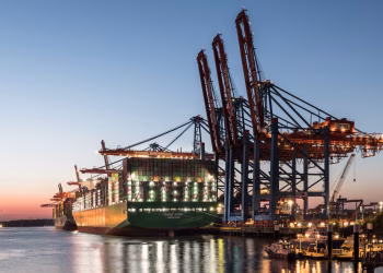 A large container ship at the Hamburg port with cranes during twilight, showcasing global trade.