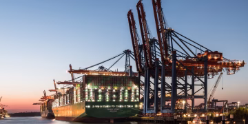 A large container ship at the Hamburg port with cranes during twilight, showcasing global trade.