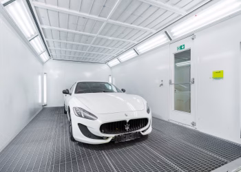 White luxury car inside a well-lit paint booth, showcasing sleek design and sophistication.
