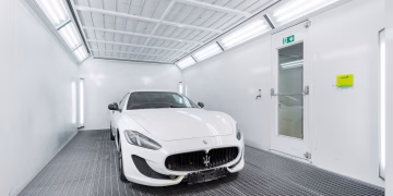 White luxury car inside a well-lit paint booth, showcasing sleek design and sophistication.