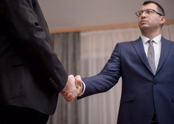 Two businessmen in formal attire shaking hands during a meeting.