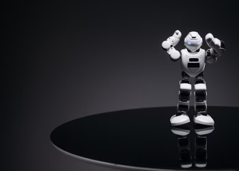 A small humanoid robot with glowing eyes on a reflective table in a dark setting.