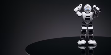 A small humanoid robot with glowing eyes on a reflective table in a dark setting.