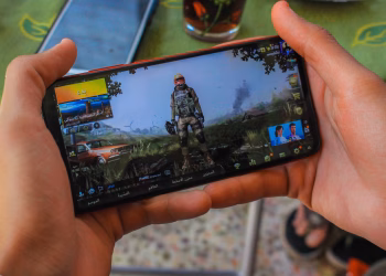 From above crop anonymous male playing captivating video game on contemporary mobile phone near table on terrace