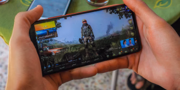 From above crop anonymous male playing captivating video game on contemporary mobile phone near table on terrace