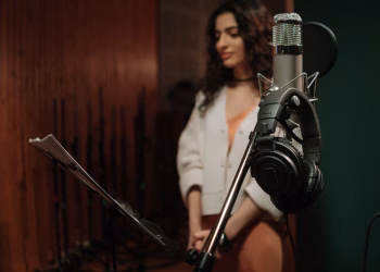 A woman stands in a recording studio, focusing on audio production with a prominent microphone.