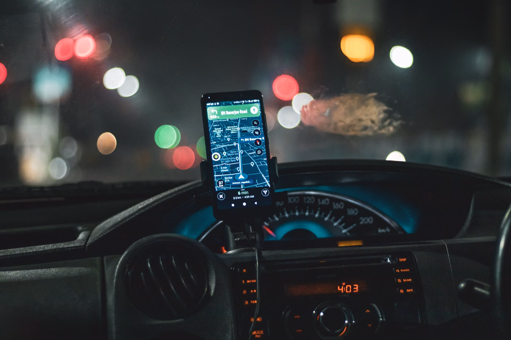 Close-up of a smartphone with map navigation in a car at night with bokeh effect.