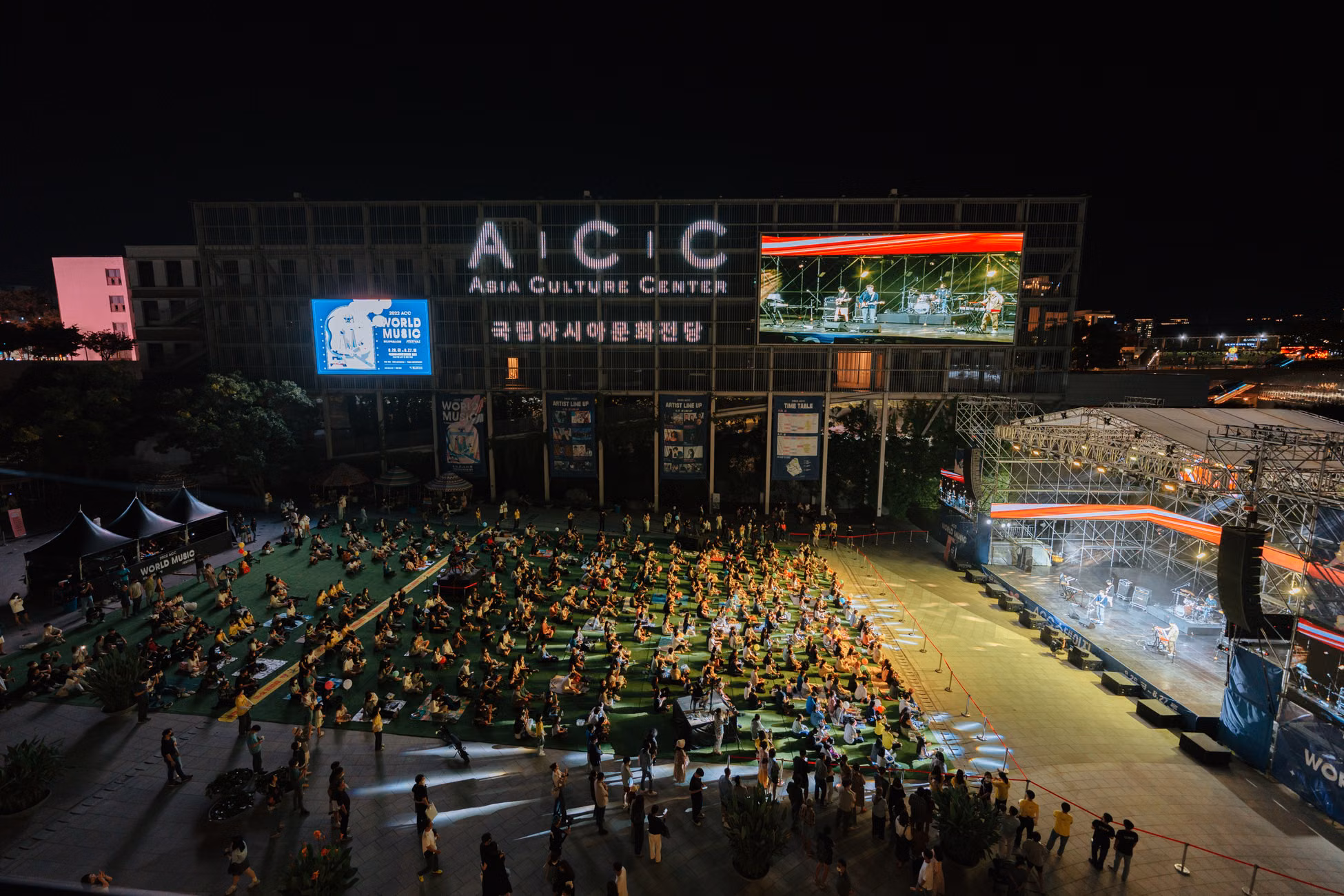 A vibrant outdoor concert at the Asia Culture Center, bustling with a lively crowd at night.